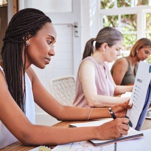 Black woman with business documents, writing at desk and women working together on audit report at