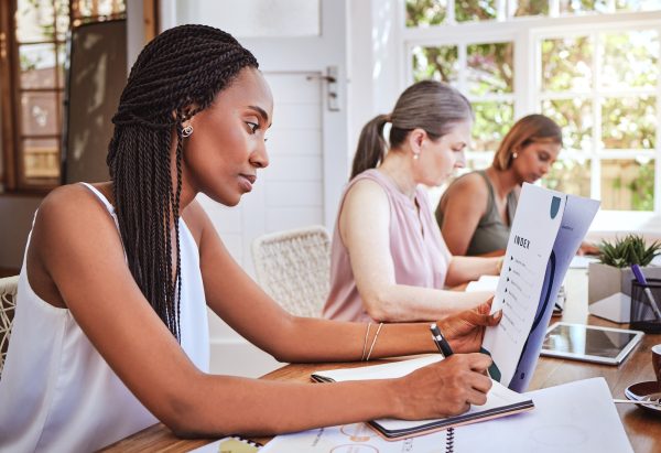 Black woman with business documents, writing at desk and women working together on audit report at