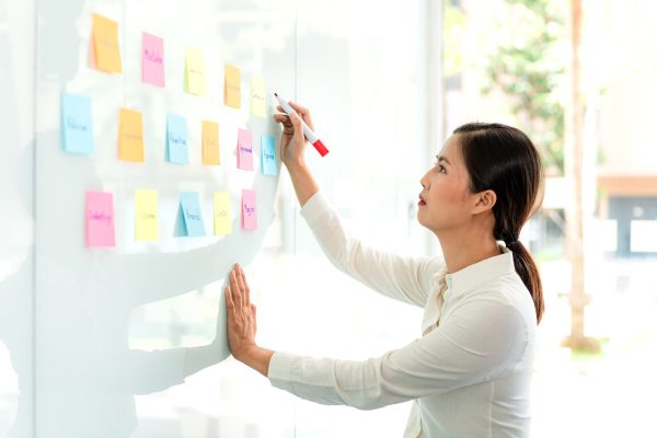 Businesswoman executive writing and taking notes keyword on board wall to planning about a business