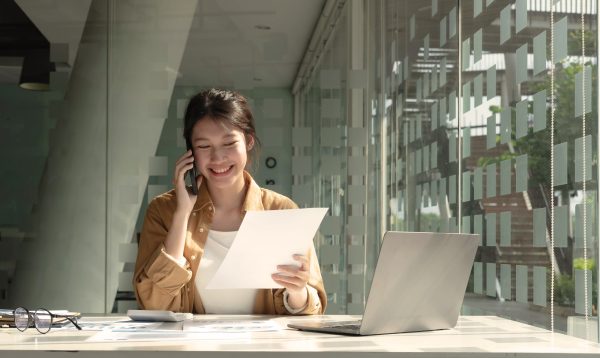 Charming Asian woman with a smile standing holding papers and mobile phone at the office.