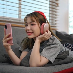 Cheerful young woman resting on couch and using mobile phone, spending time in social media.