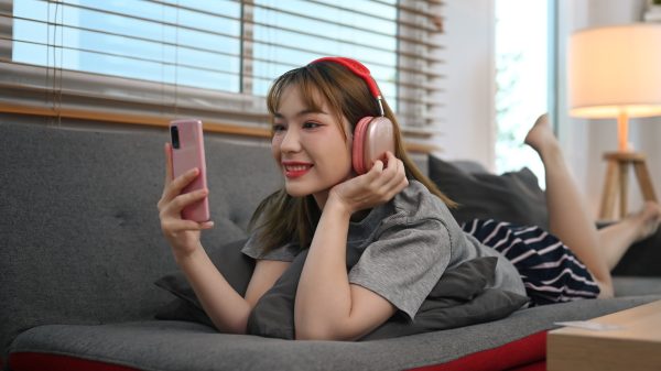 Cheerful young woman resting on couch and using mobile phone, spending time in social media.