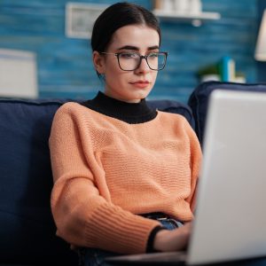 Programmer with glasses holding laptop on sofa writting code