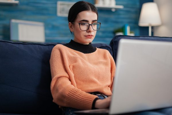 Programmer with glasses holding laptop on sofa writting code