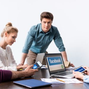 Young businesspeople using digital devices with facebook logo icons on screens