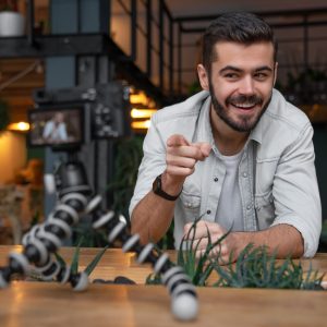 Young male blogger recording video for his vlog on digital camera mounted on flexible tripod